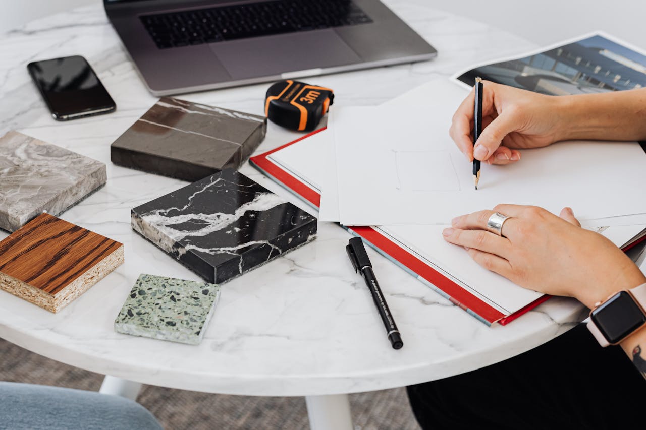 Architect works on design with material samples, sketching ideas on a marble table.