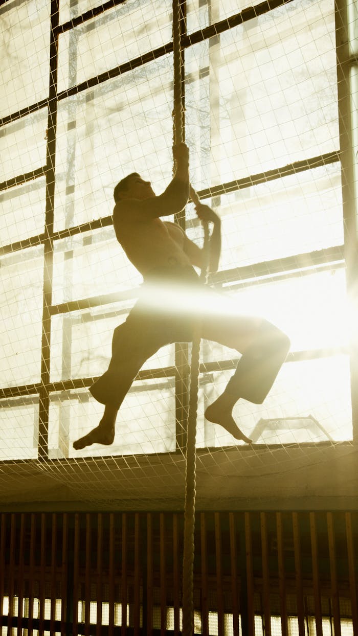 Silhouette of a man climbing a rope indoors, captured with dramatic backlight.